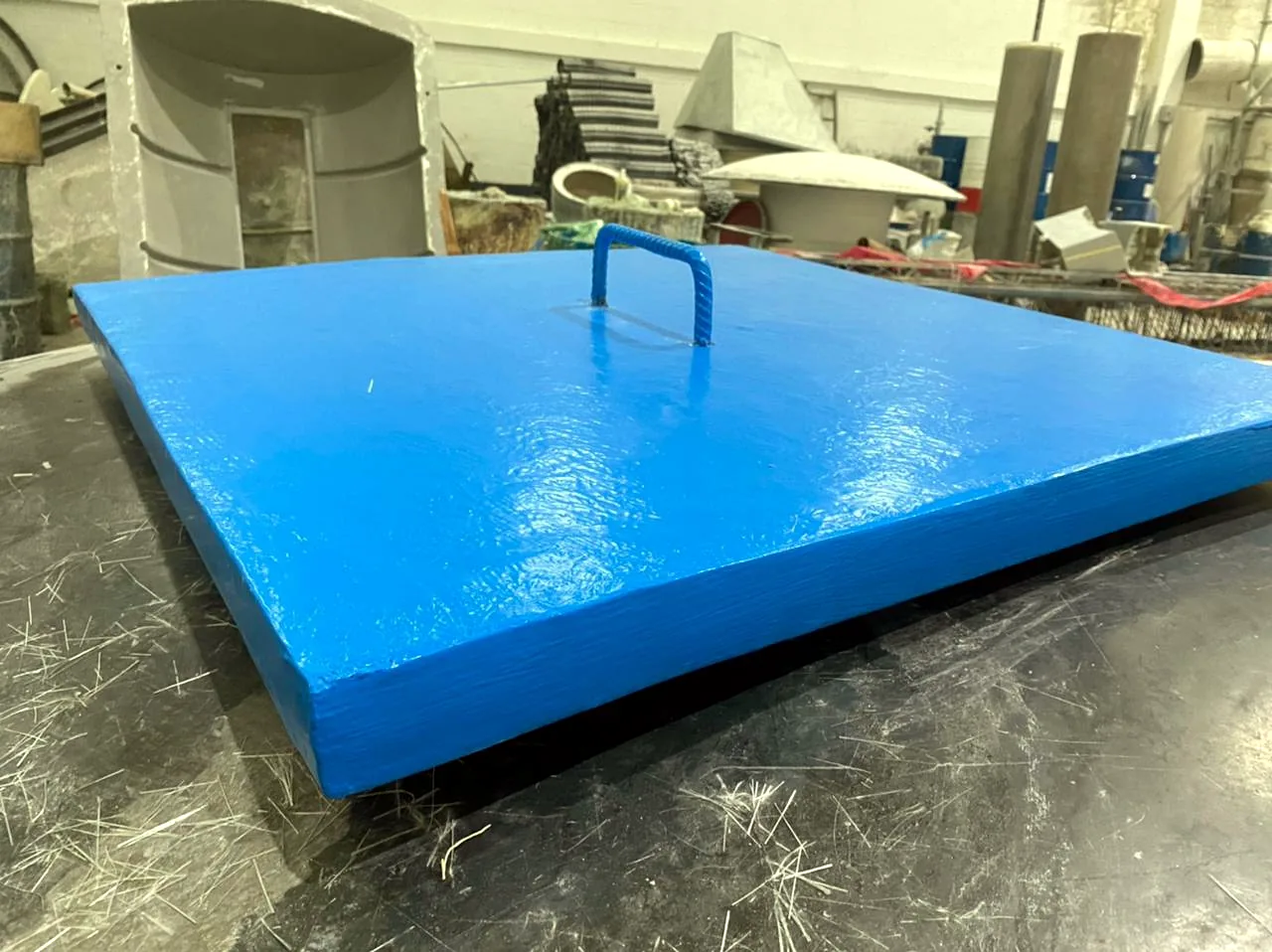 Tapa cuadrada en PRFV azul con manija laminada en el centro, terminada sobre la mesa de trabajo del taller de Fibremos Soluciones.